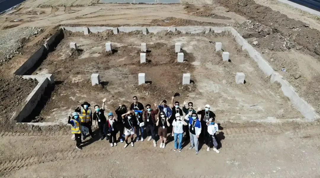 Seen from above, the team waves from a bare concrete foundation