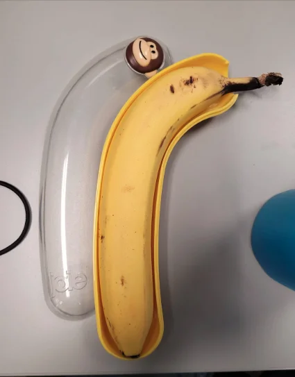 A banana lying in a yellow plastic banana case that happens to fit it