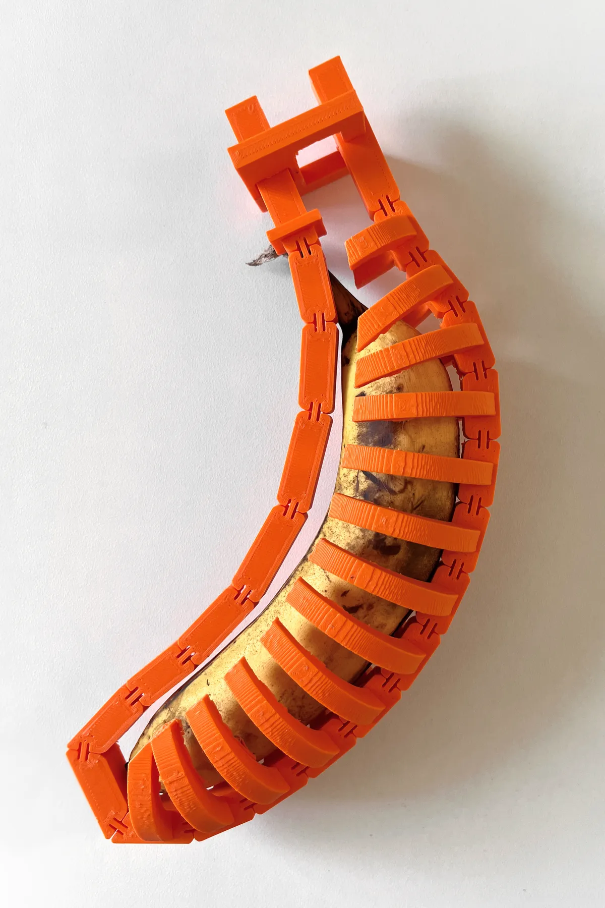 An orange 3D-printed case of ribs and spines wrapped around a ripe banana