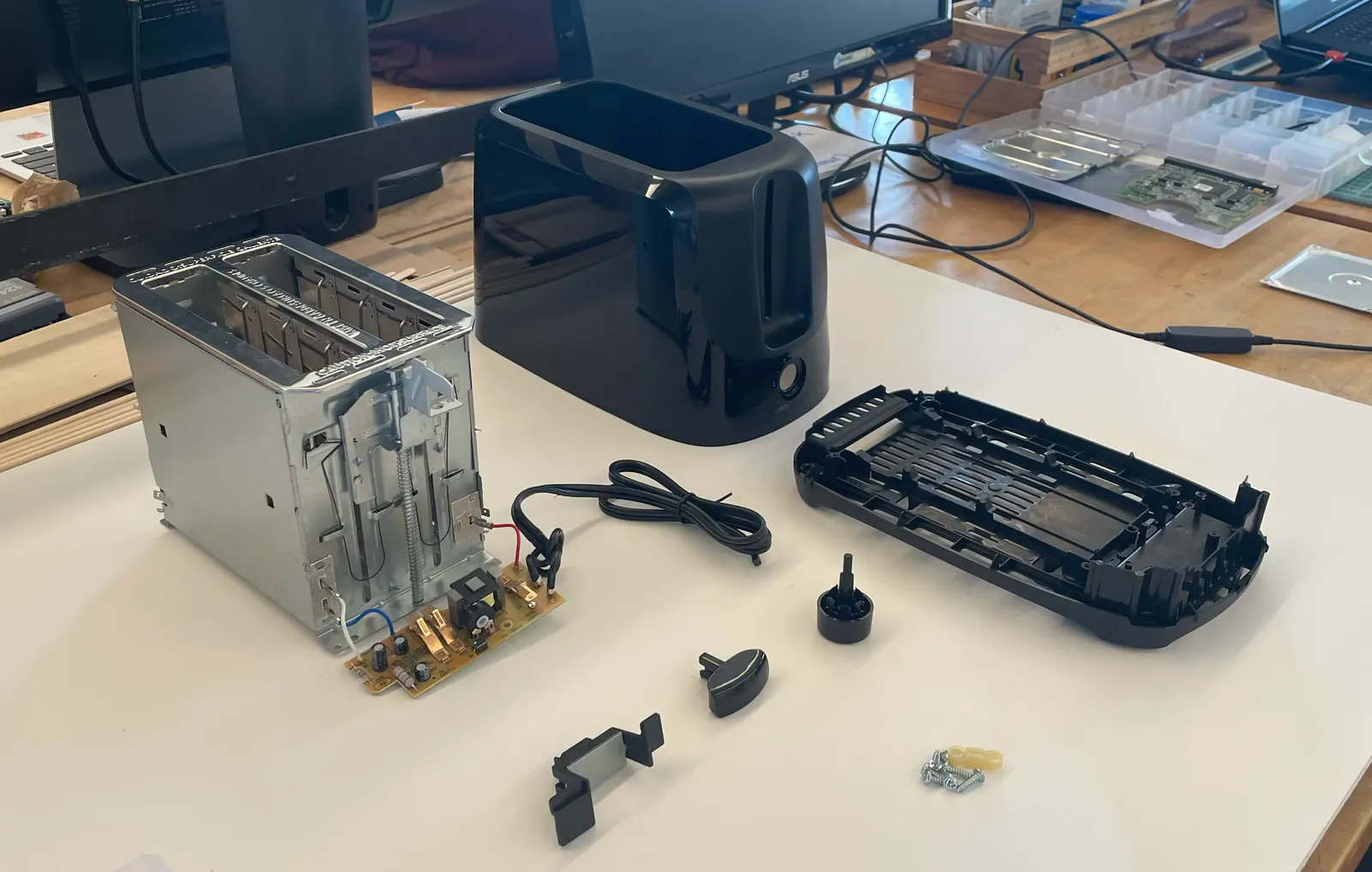 A toaster taken apart on a workbench, its shell, lever and parts laid out