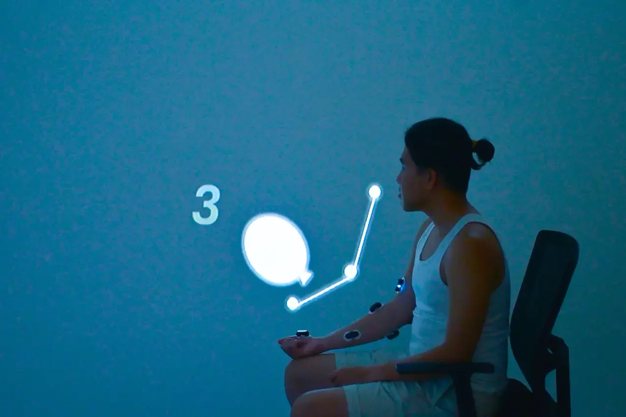 In a blue-lit room, a man raises his arm to reach a projected balloon; the count reads 3