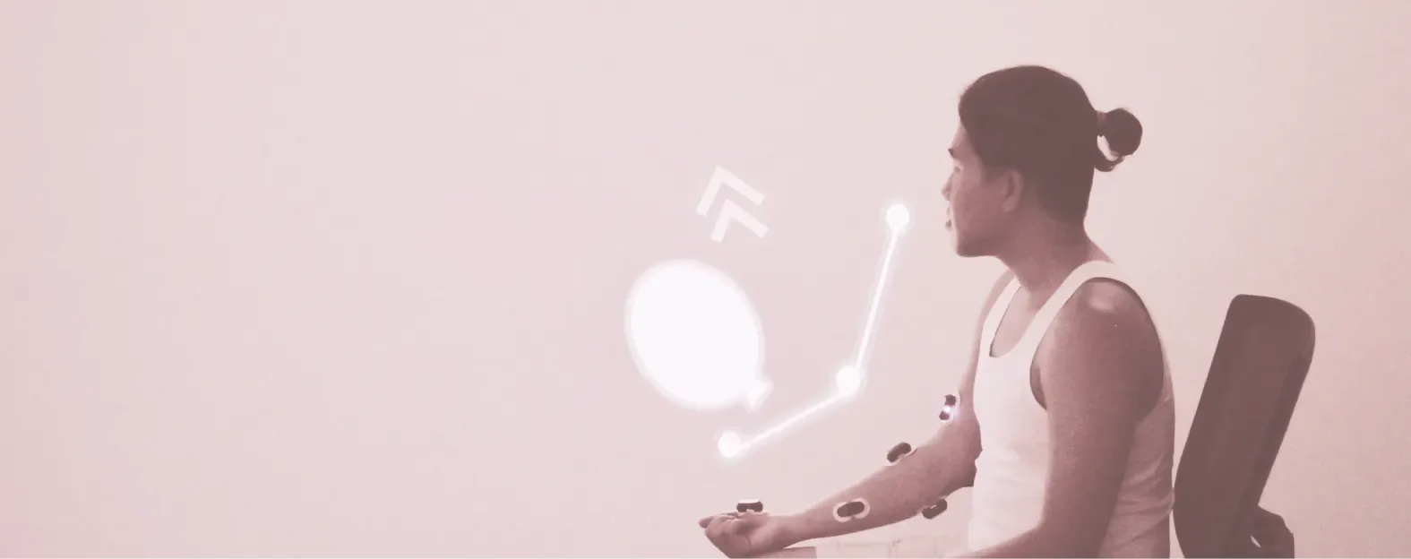 A man with sensors on his arm raises it toward a projected balloon on the wall